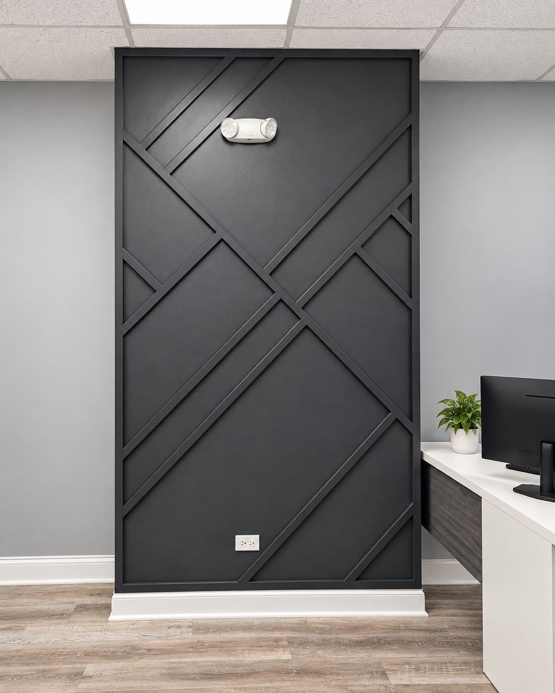 Straight-on view of a tall black geometric accent wall with a wall-mounted light fixture and outlets