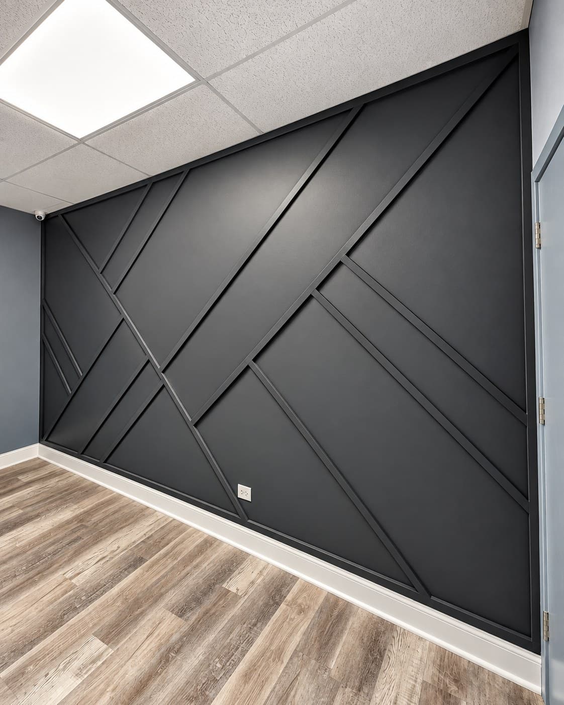 Angled view of a black geometric accent wall meeting a blue door, with a ceiling-mounted security camera