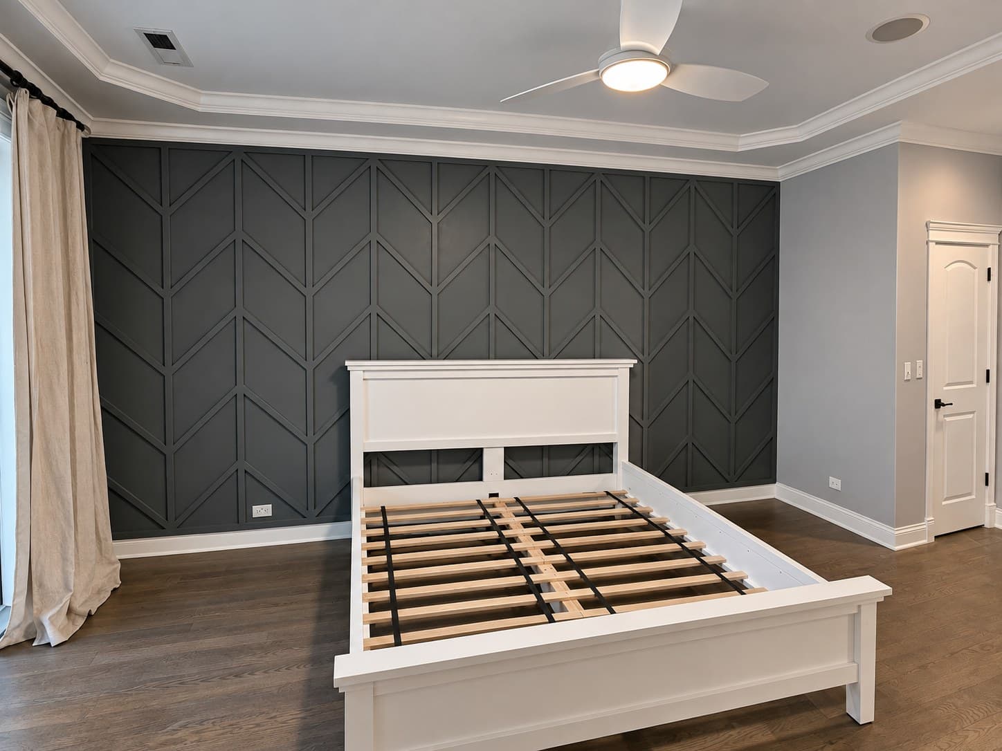 Wide view of a bedroom with a gray chevron board & batten accent wall and a ceiling fan
