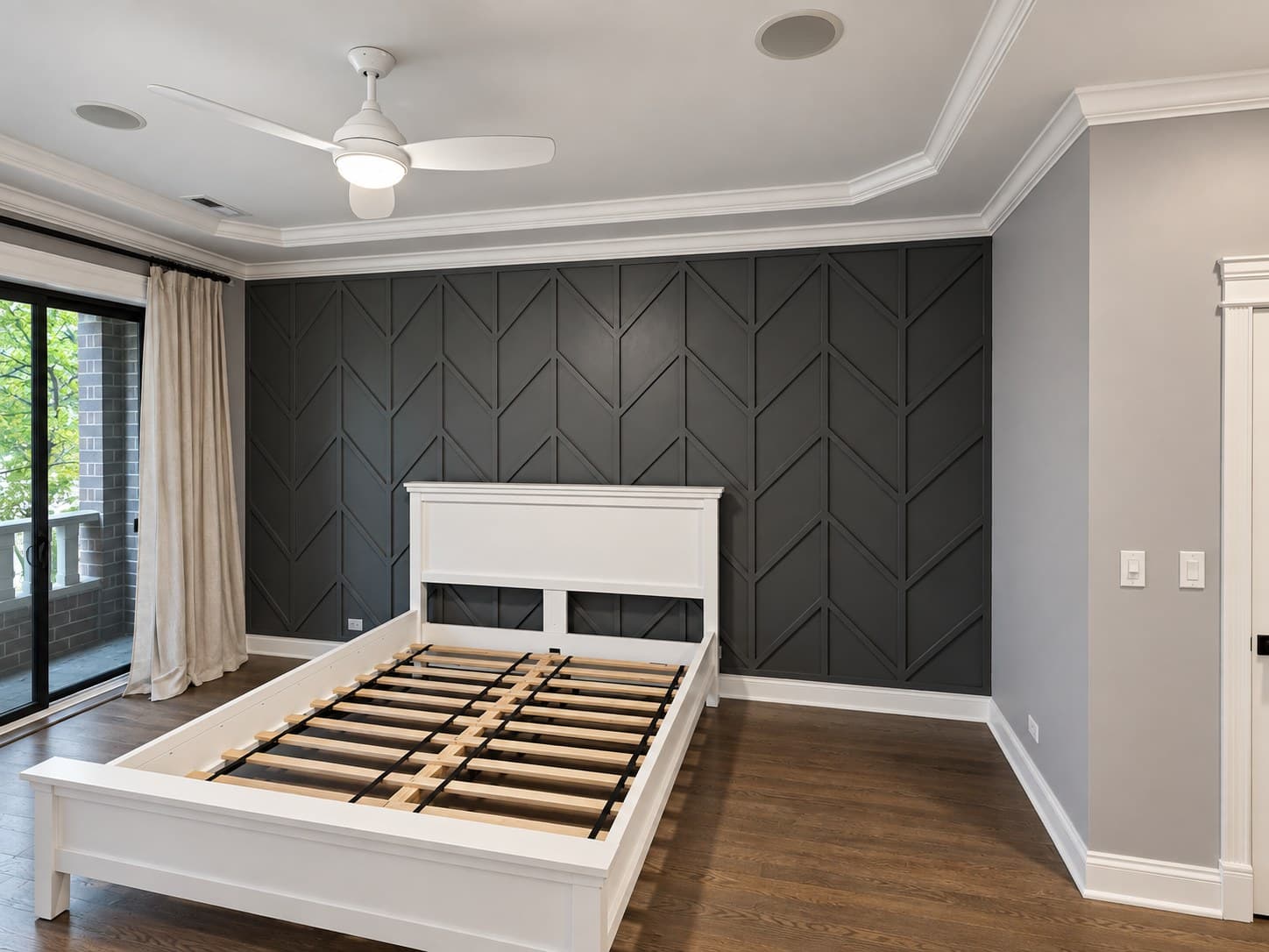 Angled view of a bedroom with a gray chevron accent wall, sliding glass door, and bed frame