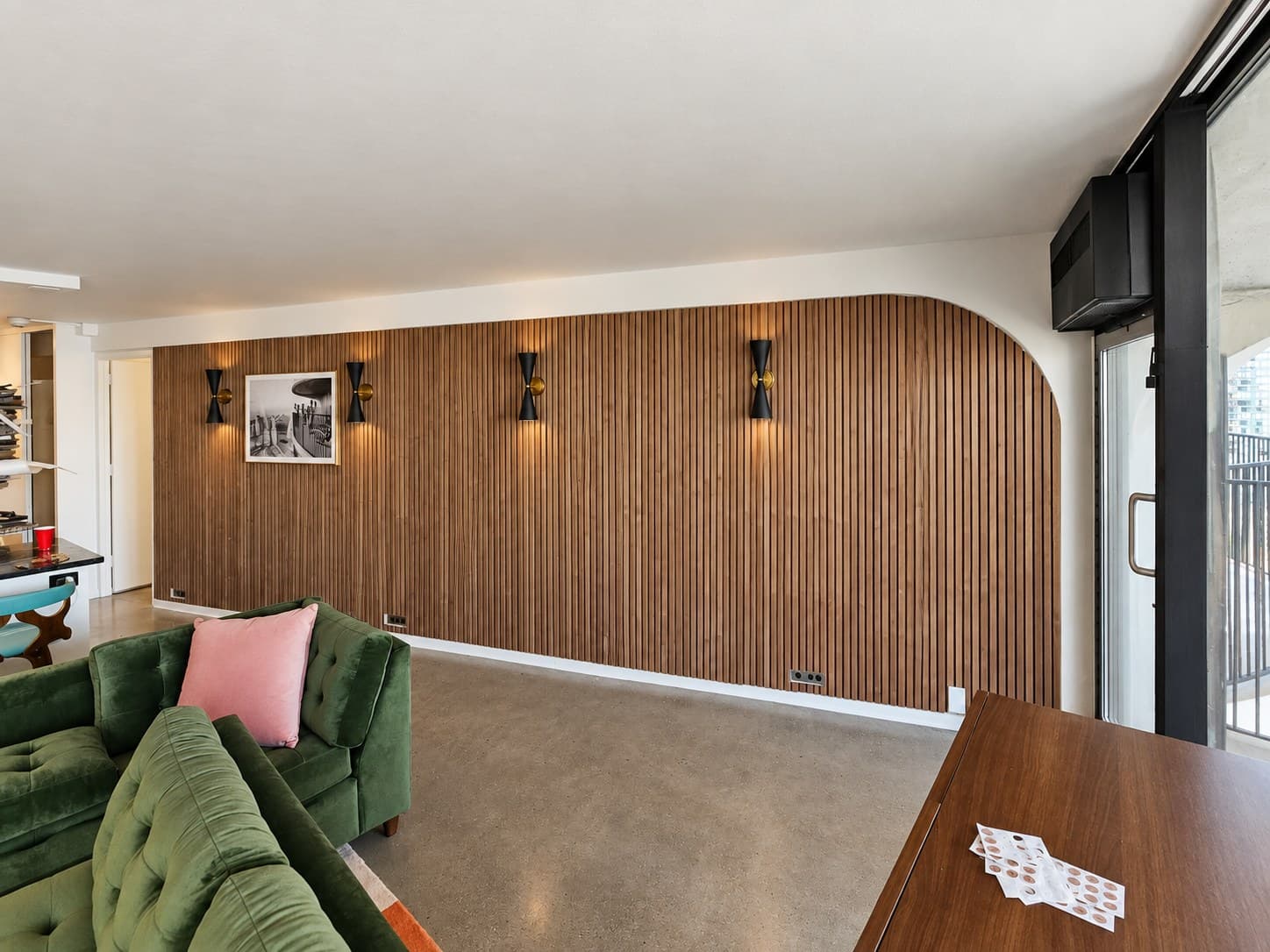 Angled view of a walnut wood slat wall and green sectional, with a patio door at the curved end