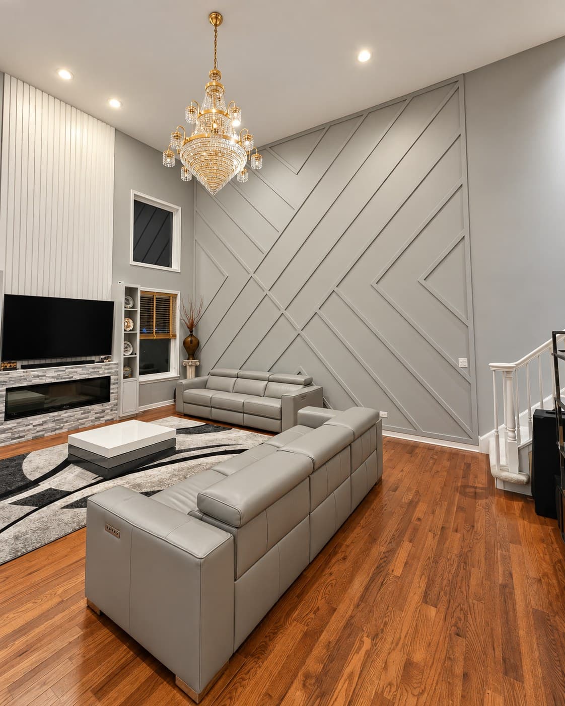 Wide view of a two-story living room with a gray geometric accent wall and a white slat fireplace wall