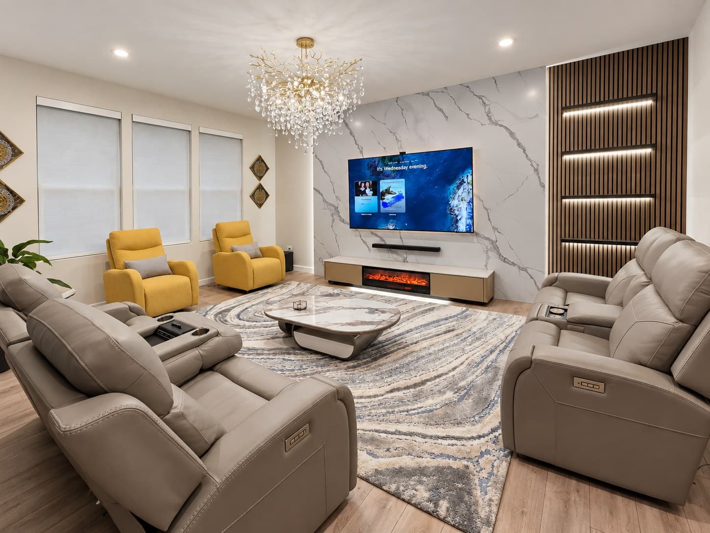 Wide view of a home theater with a marble-look media wall, gold chandelier, and yellow armchairs