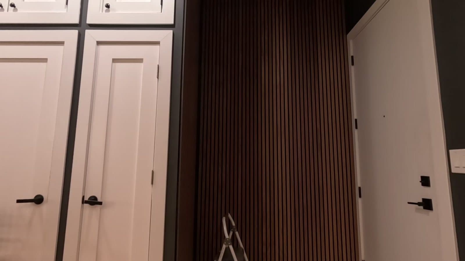 Floor-to-ceiling walnut wood slat acoustic panels in a dark entry niche between white closet doors