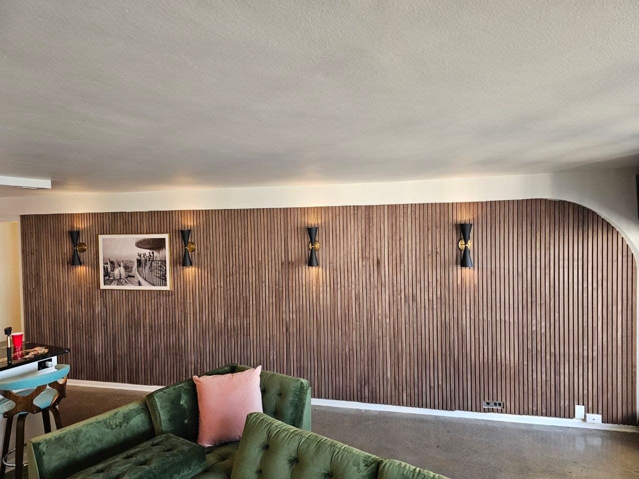 Walnut wood slat accent wall with wall sconces above a green sectional