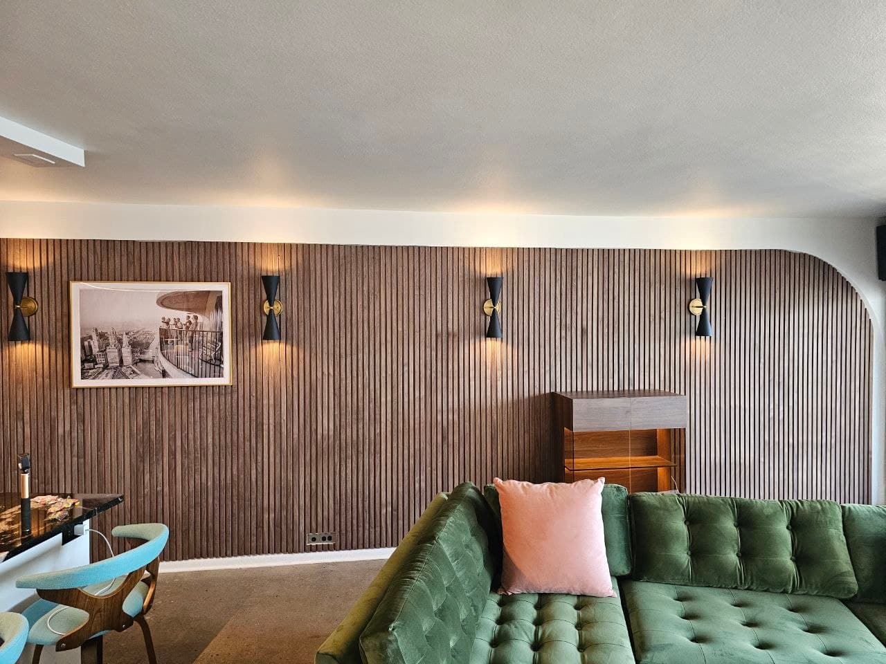 Walnut wood slat accent wall curving around a media niche, with sconces